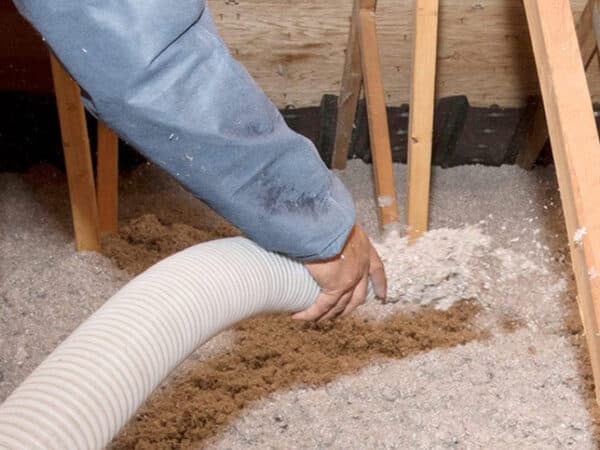 Loose-fill insulation being blown into an attic around wood framing.
