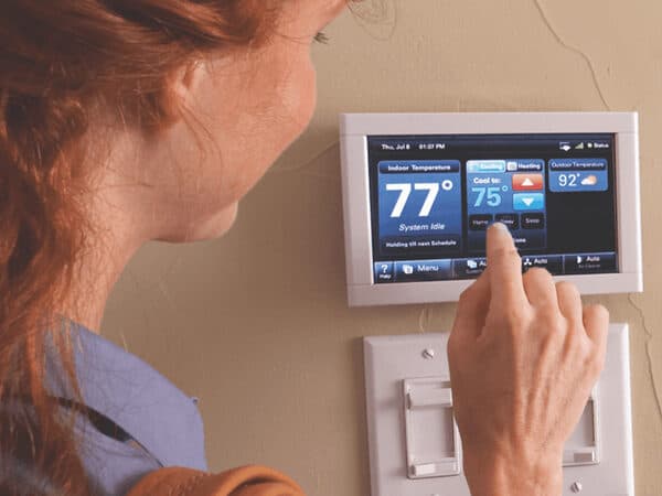 Person adjusting a wall-mounted touchscreen thermostat.